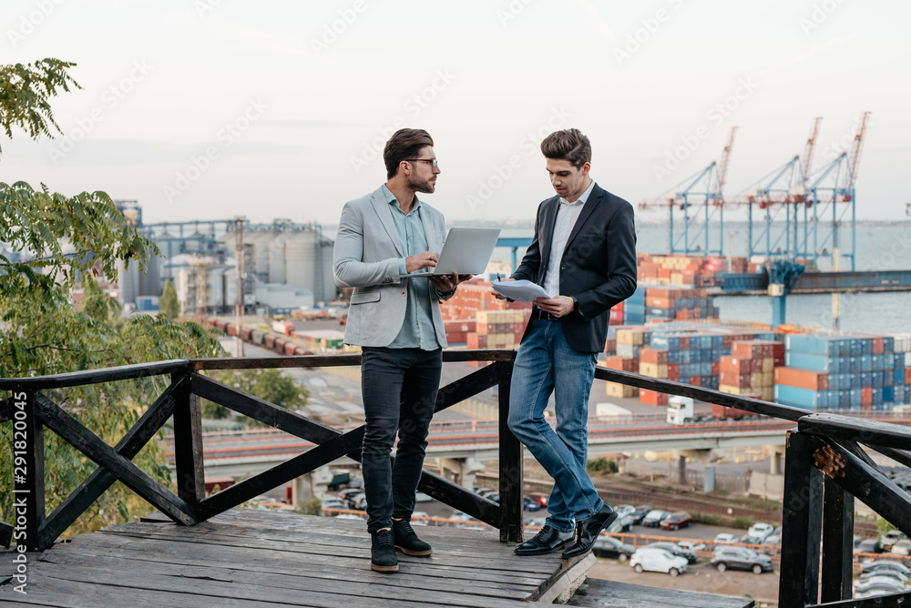 Wall mural Two business partners discussing the meeting with laptop and contract, outdoor on background of the seaport