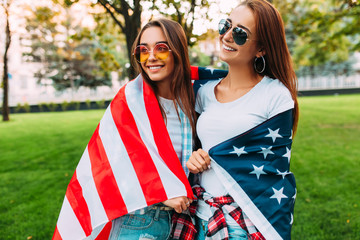 Portrait of two beautiful girls holding an American flag celebrating U.S. independence day fun in...