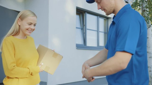 Beautiful Young Woman Meets Delivery Man who Gives Her Cardboard Box Package, She Signs Electronic Signature POD Device. Courier Delivering Parcel in the Suburban Neighborhood. In Slow Motion