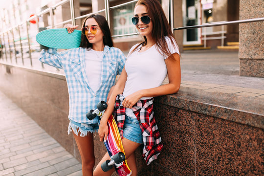 Two attractive young girls in sunglasses pose with skateboards in the city