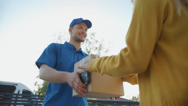 Beautiful Young Woman Meets Delivery Man who Gives Her Cardboard Box Package, She Signs Electronic Signature POD Device. Courier Delivering Parcel in the Suburban Neighborhood. Slow Motion Low Angle 
