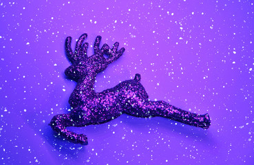 Obraz na płótnie Canvas Christmas deer on violet sparkling background with snow.