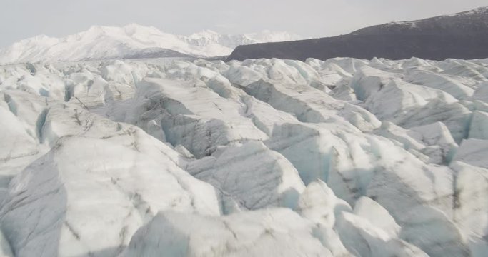 Aerial shot, day, low fly over jagged glacier top in valley, mountains in distance, drone