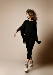 New pretty modern style dancer curly hair woman dancing posing in designer black cloth full body on beige background