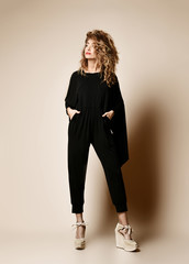 New pretty modern style dancer curly hair woman dancing posing in designer black cloth full body on beige background