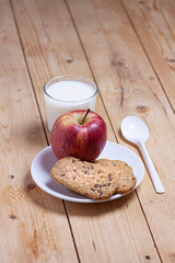 BREAKFAST WITH GLASS OF MILK, APPLE AND COOKIES WITH CHOCOLATE CHIPS ON WOODEN TABLE. HEALTHY FOOD