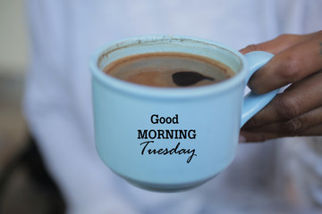 Cup of coffee in hand. Good morning Tuesday greeting on cup of coffee. Morning coffee concept.