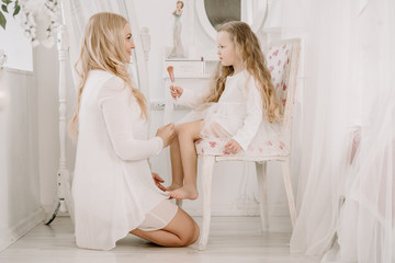 Beautiful woman and child girl doing make up each other on white room background