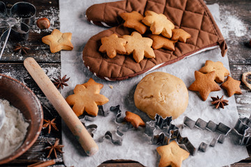 Freshly baked appetizing homemade gingerbread cookies, raw dough, baking utensils and food decorations. Christmas and New Year celebration traditions. Family home bakery, cooking festive sweets