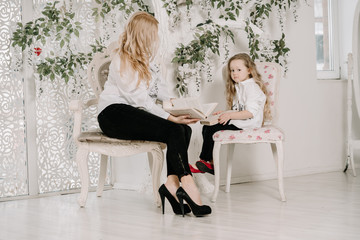 Portrait Of Mother And Daughter Indoors happy sitting near and reading books together indoors in white room