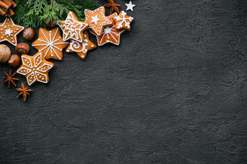 Christmas background with homemade gingerbread cookies, evergreen branches and decorations on black table. Festive food, New Year celebration traditions