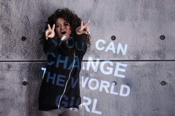Naklejka na ściany i meble Curly girl dances against the background of gray wall onto which a multi colored motivational inscription is projected.