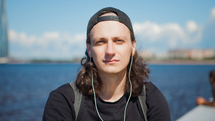 Portret of a young man sitting on the embankment with against the sky, clouds, sea, and modern urban architecture. © Ulia Koltyrina