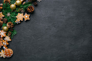 Christmas background with homemade gingerbread cookies, evergreen branches and decorations on black table. Festive food, New Year celebration traditions