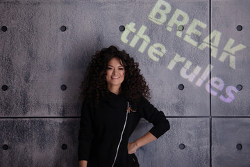 Curly young woman in a strong, boxing pose against a concrete wall background. Colored light sign...