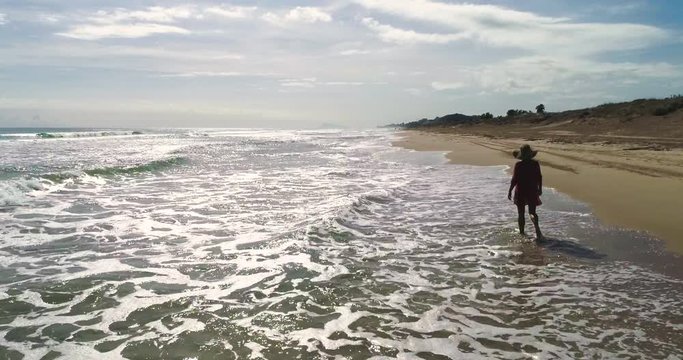 Dron vuela sobre el mar y chica paseando en la orilla