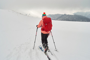 Woman ski touring on an overcast day with poor visibility, in Baiului mountains, Romania - view from behind.