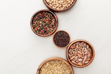 top view of wooden bowls with black quinoa, oatmeal, beans, peppercorns and chickpea on white...