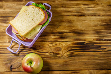 Lunch box with sandwiches and apple on a wooden table. Top view, copy space