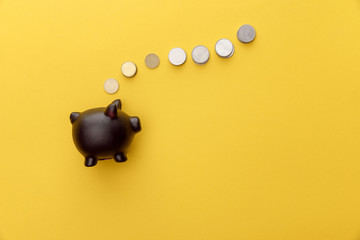 top view of black piggy bank with coins on yellow background