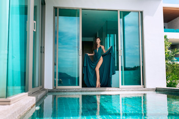 Beautiful brunette in blue evening dress posing standing near the pool in a villa