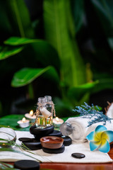 Two jars of aromatic oils standing on stones for a therapy stone and located on a terry towel next to which a flower lies, there are transparent spheres a rolled towel and a sprig of lavender