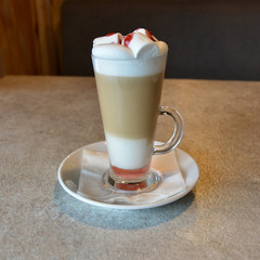 Latte with marshmallow and raspberry syrup. Glass cup of coffee latte on a table in a cafe. Delicious coffee. Stylish view. Closeup.