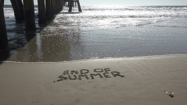 Wave rolling up to the words End of Summer written in the sand on a beautiful tropical beach