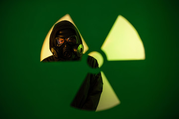 A man standing in a dark hoodie with a hood on his head with a gas mask on his face standing near...