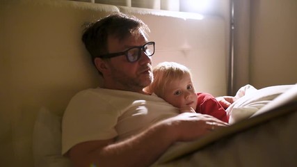 Father reading bedtime stories to child. Dad putting son to sleep. Quality family time.