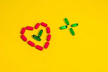 Green transparent capsules folded in the form of a cross next to the heart of the capsules in the center of which lies a pair of green capsules on a yellow background. Medicine concept.