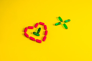 Green transparent capsules folded in the form of a cross next to a heart from capsules on a yellow background.The concept of pharmacology.