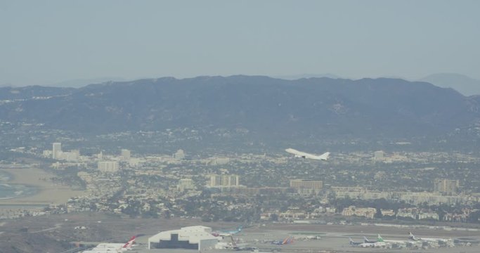 Aerial shot, day, distant side view of plane taking off from LAX towards sea, drone