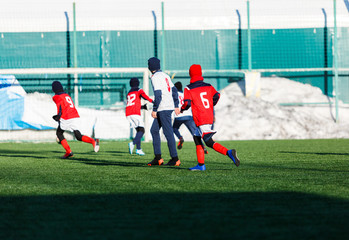 Fototapeta premium Boys in white and red sportswear plays football on field, dribbles ball. Young soccer players with ball on green grass. Training, football, active lifestyle for kids , winter sport
