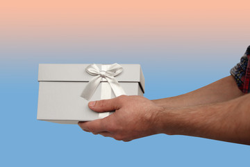 man holding a gift in a light gray box with a satin ribbon and a bow, the concept of Valentine's Day, Christmas presents, mother's day, new year, close-up, copy space