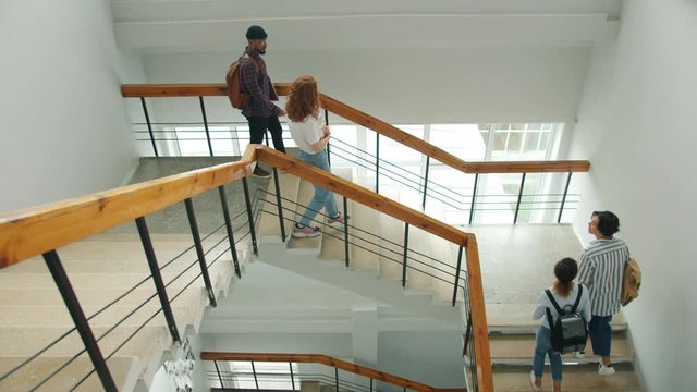 Cheerful Students Friends Are Meeting On Stairs In University Doing High-five Chatting Walking Together. Education, Friendship And Campus Interior Concept.