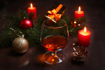 christmas decoration with glass of cognac or whiskey, red candles, gift box and christmas tree. Selective focus.