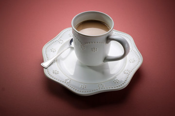 Coffee with cream in white coffee cup resting on large white saucer with spoon