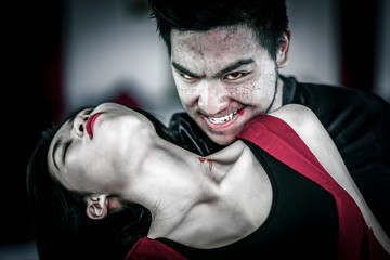 Close up of male vampire in black hood biting a beautiful lady. Halloween concept.