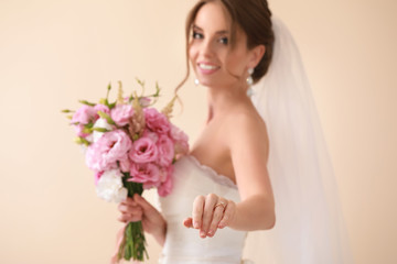 Beautiful young bride with wedding bouquet showing ring against light background