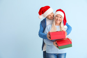 Happy mature couple with Christmas gifts on light background