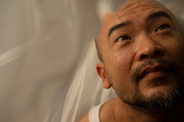 portrait of 40 Japanese adult man wake up in the early morning light with white soft fabric shadow on the face