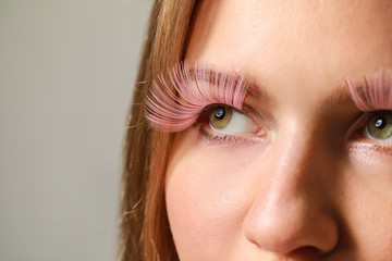 Young woman with creative eyelashes on grey background, closeup