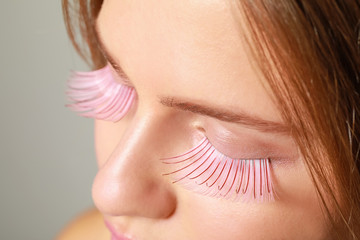 Young woman with creative eyelashes on grey background, closeup