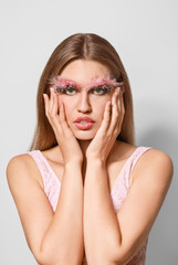 Young woman with creative eyelashes and eyebrows on grey background