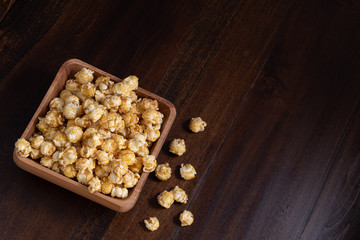 Caramel Popcorn Spilling out of a Wooden Bowl onto a Brown Table