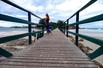 Mujer en puente de madera q<sobre el mar que lleva a una isla