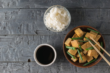 Fototapeta na wymiar Grilled tofu cheese with green onions, rice and soy sauce on a wooden table. Flat lay.
