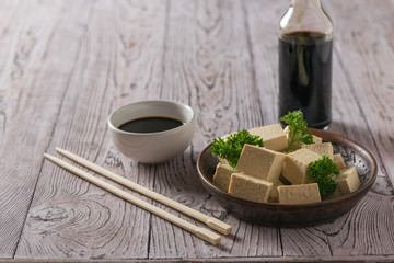 A bottle of soy sauce and slices of tofu cheese on a wooden table. Soy cheese.