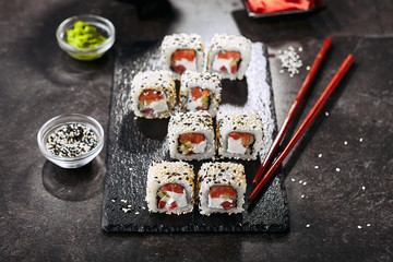 Tokyo salmon uramaki sushi with rice, cream cheese, tomatoes, cucumber, sesame and nori close up. Macro shot of japanese food uramaki rolls with smoked fish and fresh vegetables
